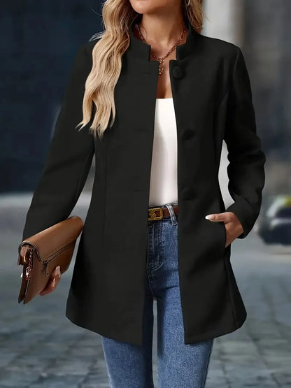 Person wearing a black coat, white shirt, blue jeans, and holding a brown handbag on a blurred street background.