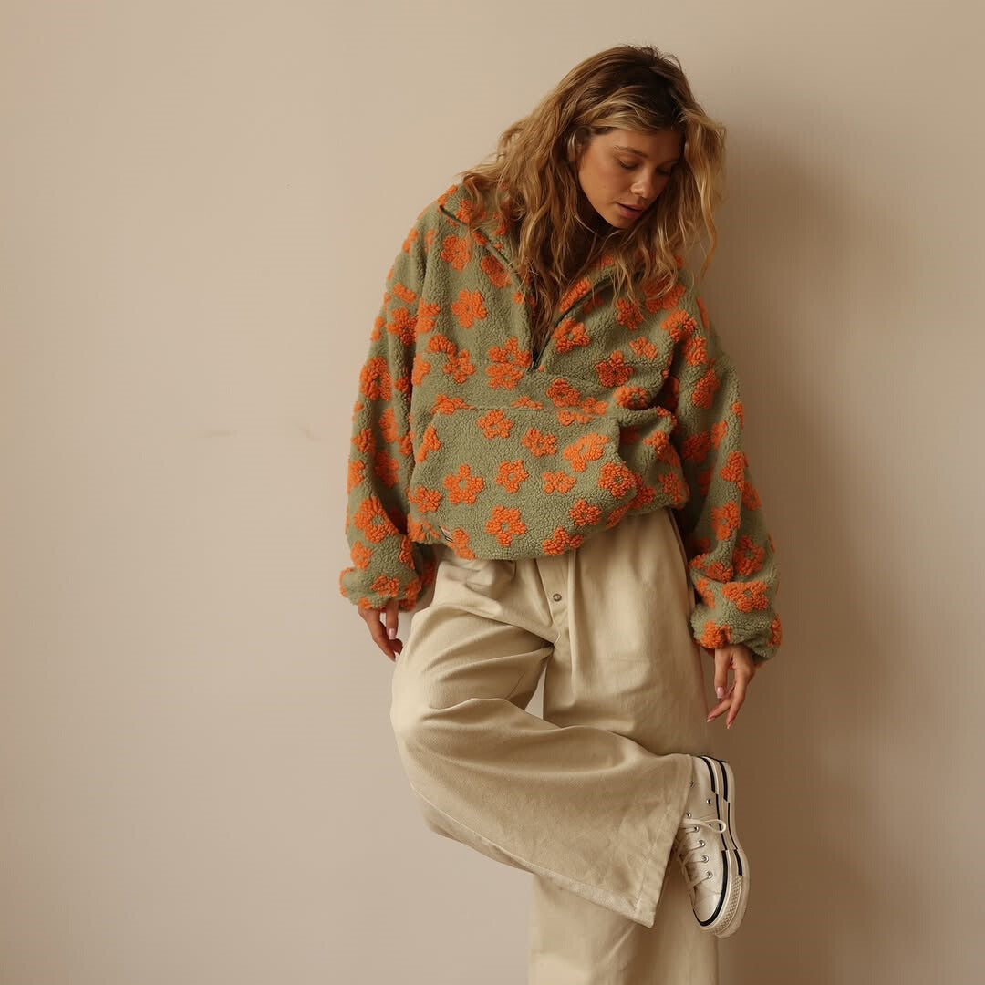 Woman wearing a green sweater with orange floral patterns against a beige background