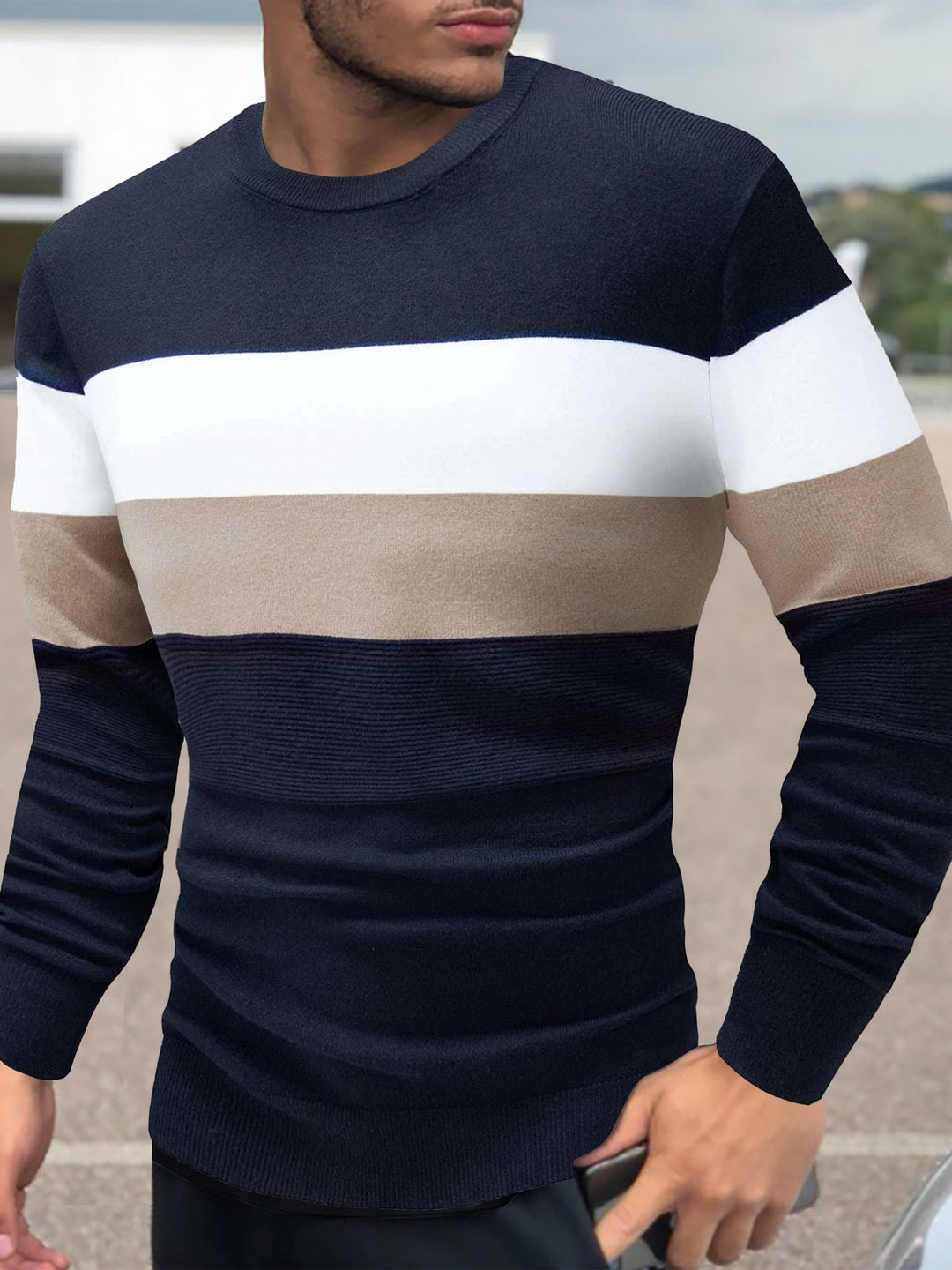 Man wearing a navy, white, and beige striped sweater outdoors.