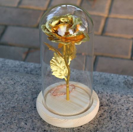 Gold rose inside a glass dome on a wooden base with a brick background