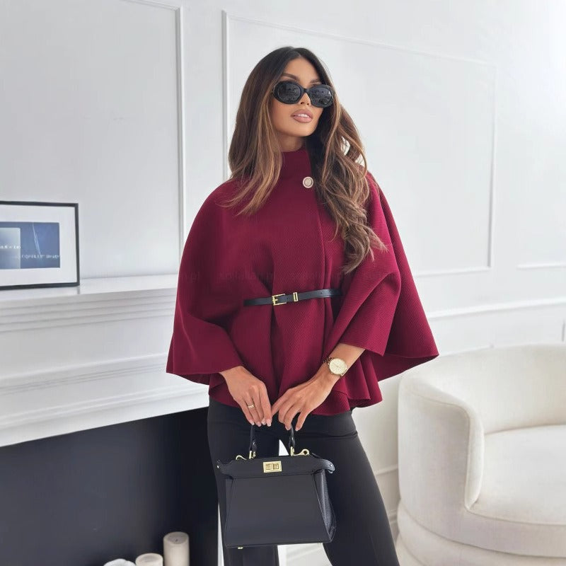 Woman in a burgundy cape holding a black handbag in a stylish room.