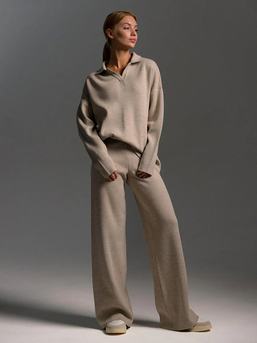 Woman wearing a beige sweater and wide-leg pants against a gray background