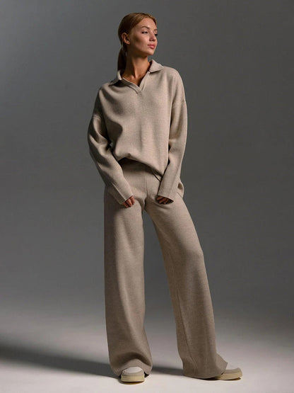 Woman wearing a beige sweater and wide-leg pants against a gray background