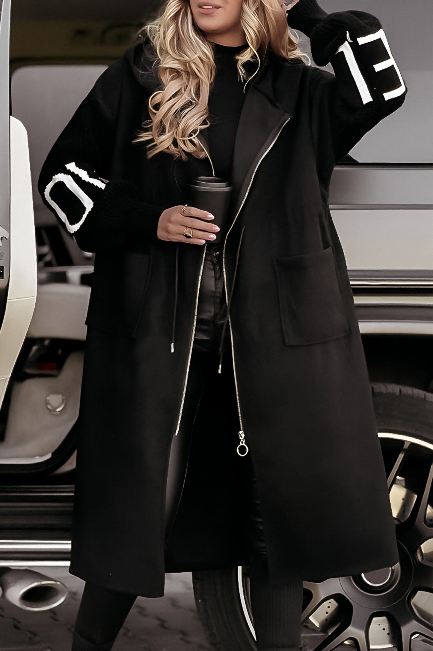 Person wearing a black coat with white lettering, standing next to a vehicle.