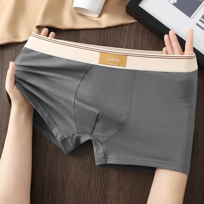 Gray underwear held by hands on a wooden surface with a beige shirt and black book in the background.