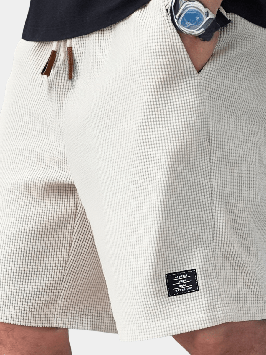 Close-up of a person wearing white checkered shorts with a brand label.