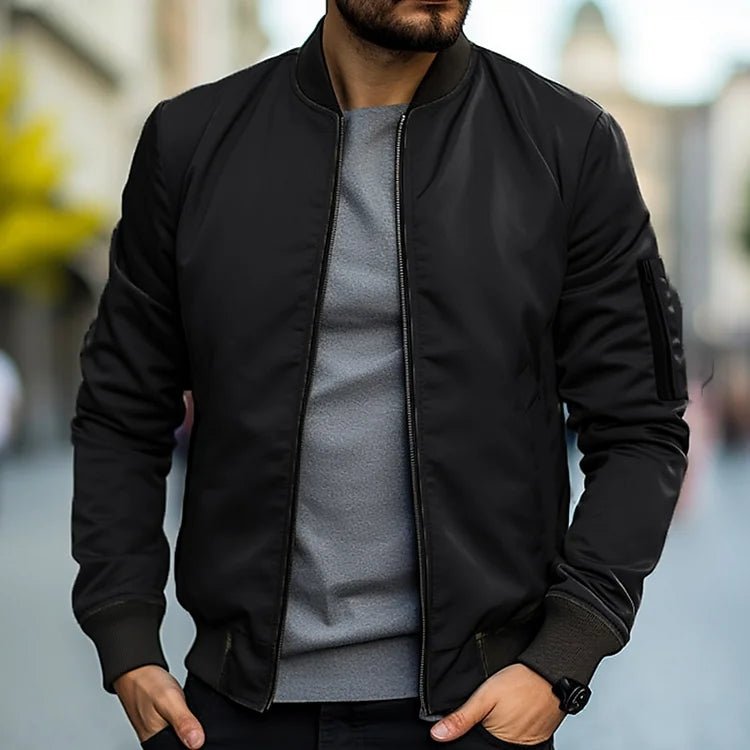 Man wearing a black bomber jacket over a gray shirt with a blurred background