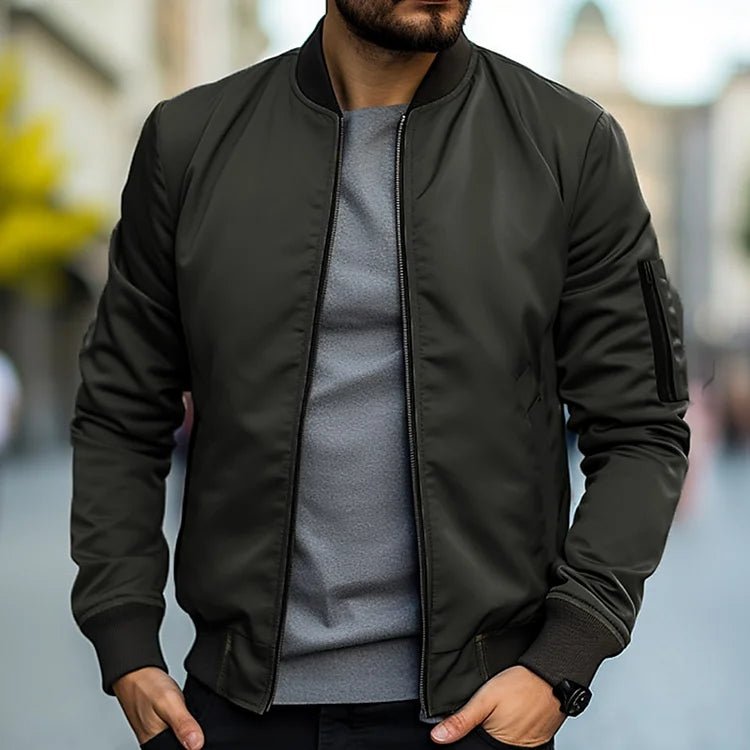 Man wearing a black bomber jacket over a gray shirt with a blurred background