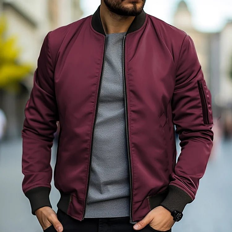 Man wearing a burgundy bomber jacket over a gray shirt with a blurred background