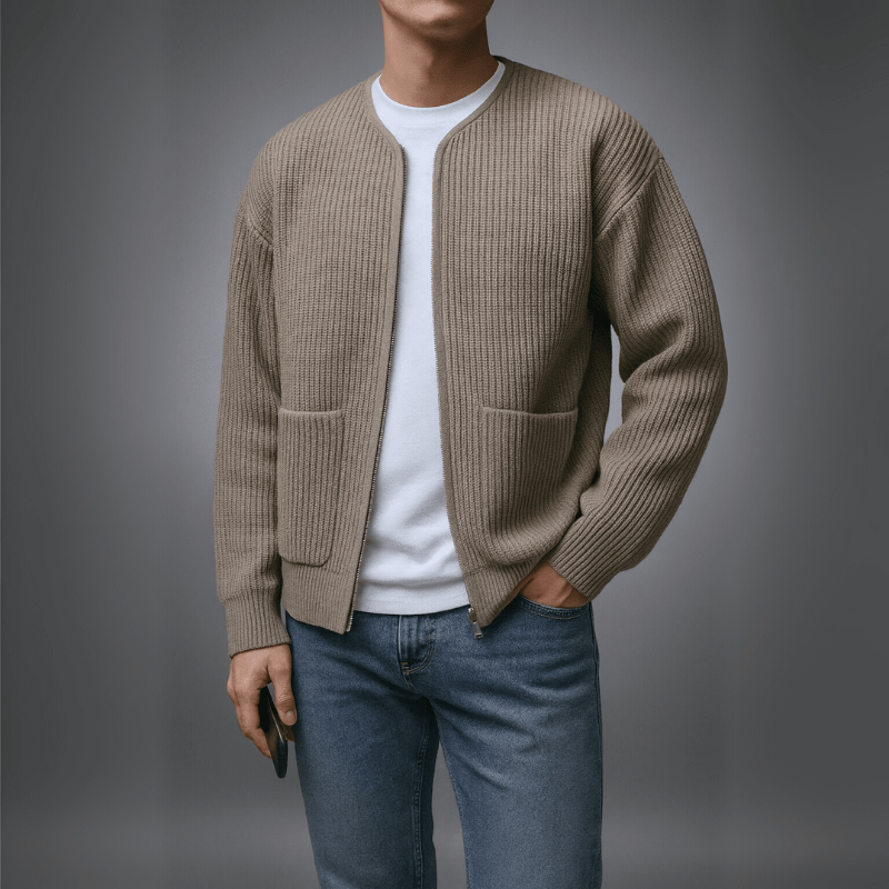 Person wearing a beige cardigan over a white shirt and blue jeans on a gray background