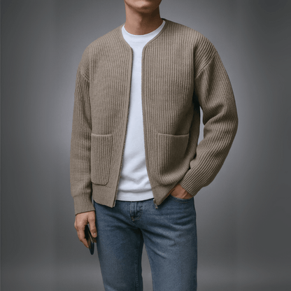 Person wearing a beige cardigan over a white shirt and blue jeans on a gray background