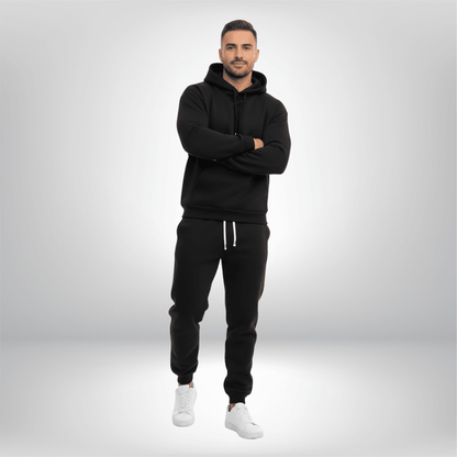 Man wearing a black hoodie and pants with white sneakers on a light gray background