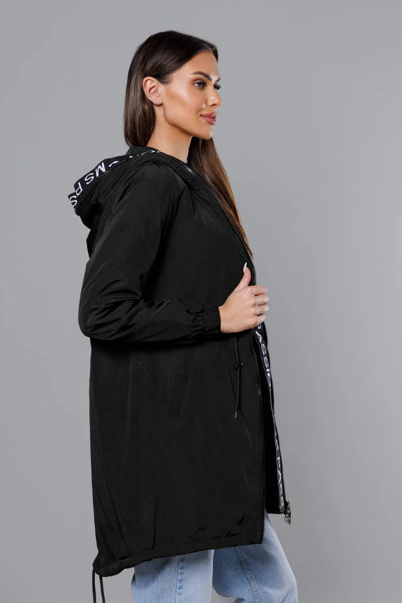 Woman wearing a black hooded jacket with text on the sleeve against a gray background