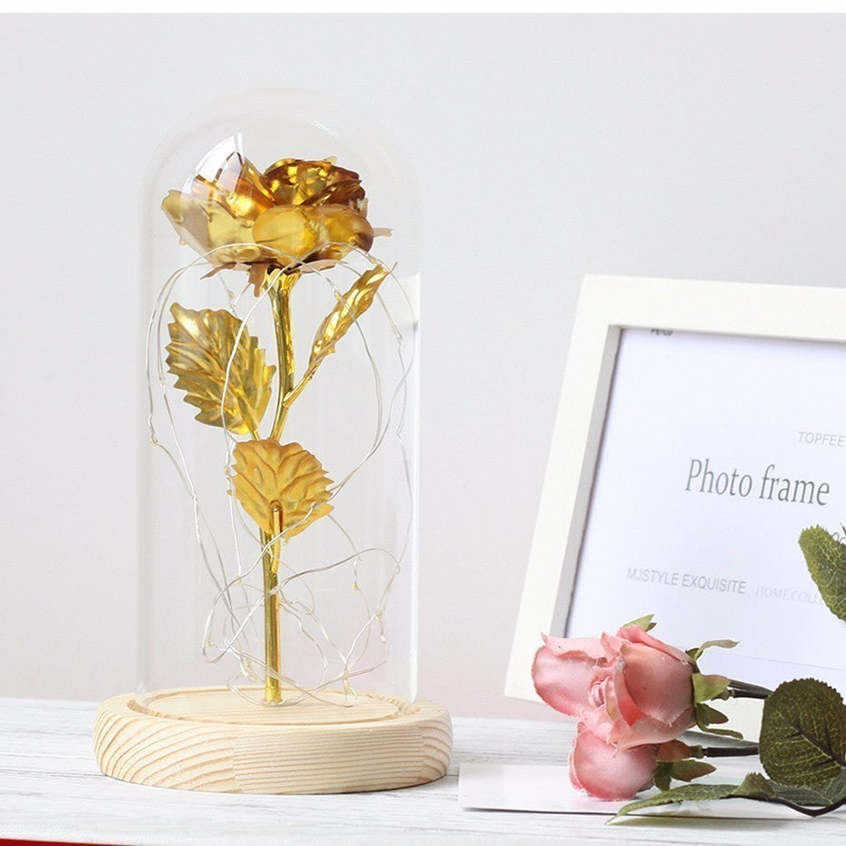 Gold rose in a glass dome on a white surface with a photo frame in the background.