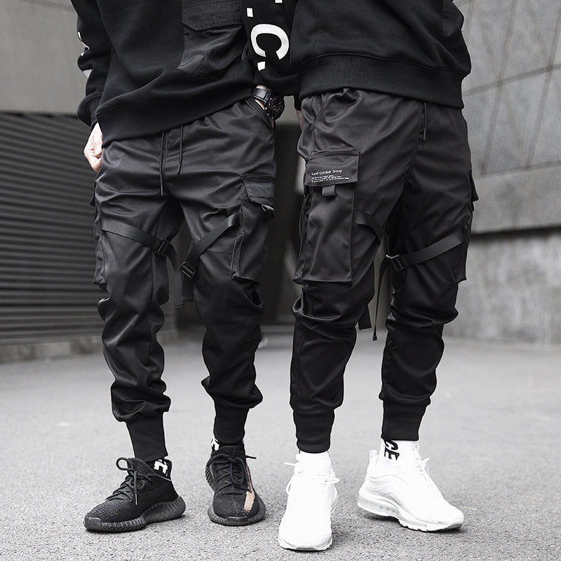 Two people wearing black cargo jogger pants and sneakers on a street.