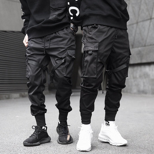 Two people wearing black cargo jogger pants and sneakers on a street.