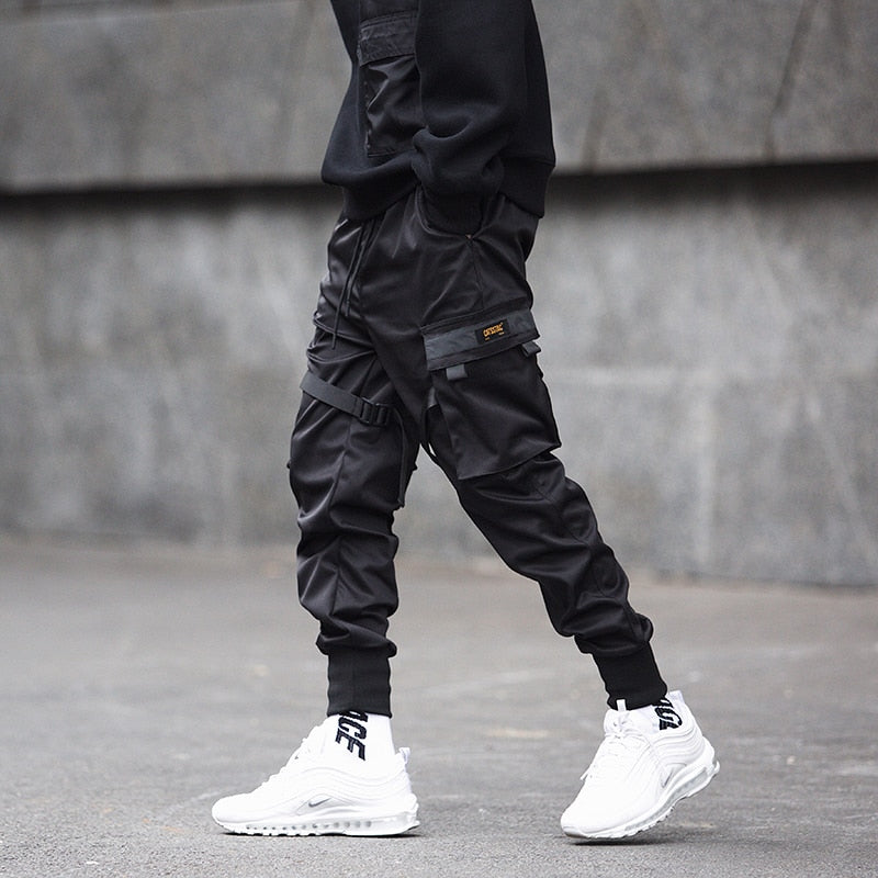 Person wearing black cargo pants and white sneakers on a gray pavement.