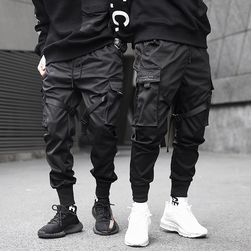 Two people wearing black cargo pants and sneakers on a gray pavement.