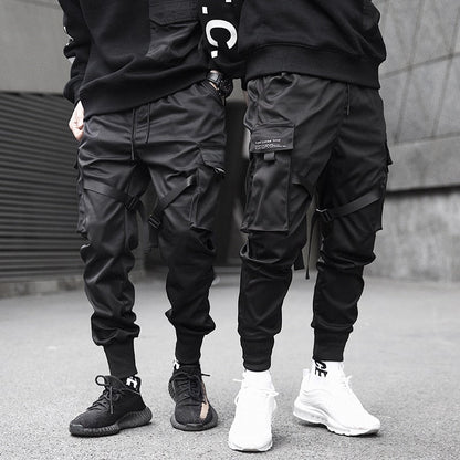 Two people wearing black cargo pants and sneakers on a gray pavement.