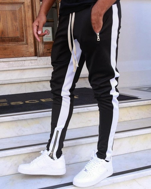 Person wearing black track pants with white stripes and white sneakers on a staircase.