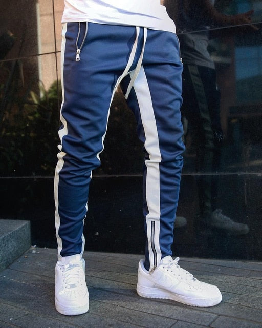 Blue jogger pants with white stripes worn by a person, standing on a reflective surface.