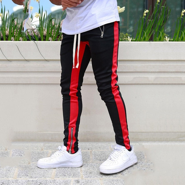 Person wearing black and red striped pants with white sneakers on a concrete surface.
