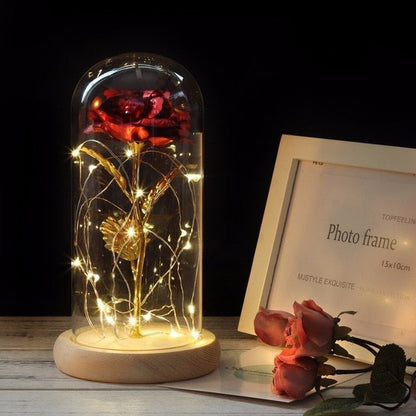 Decorative lamp with a gold-leafed rose inside a glass dome on a wooden base.