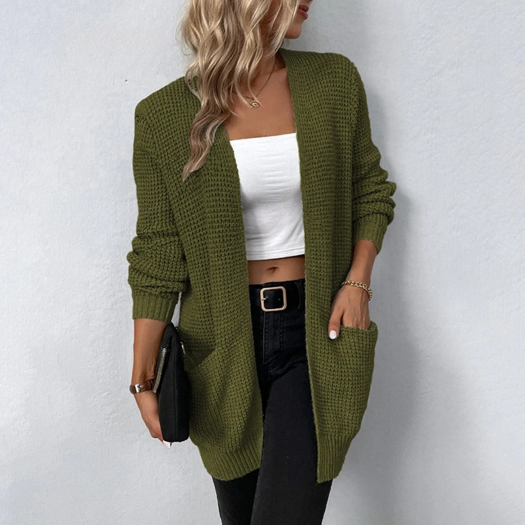 Woman wearing a green knitted cardigan over a white top and black pants against a white background