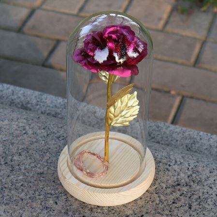 Decorative flower with gold stem under a glass dome on a wooden base.