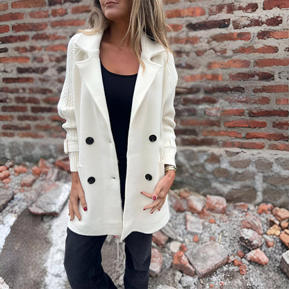 Woman wearing a white coat with black buttons against a brick wall.