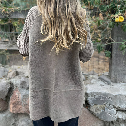 Person wearing a beige sweater with a stone wall and greenery in the background