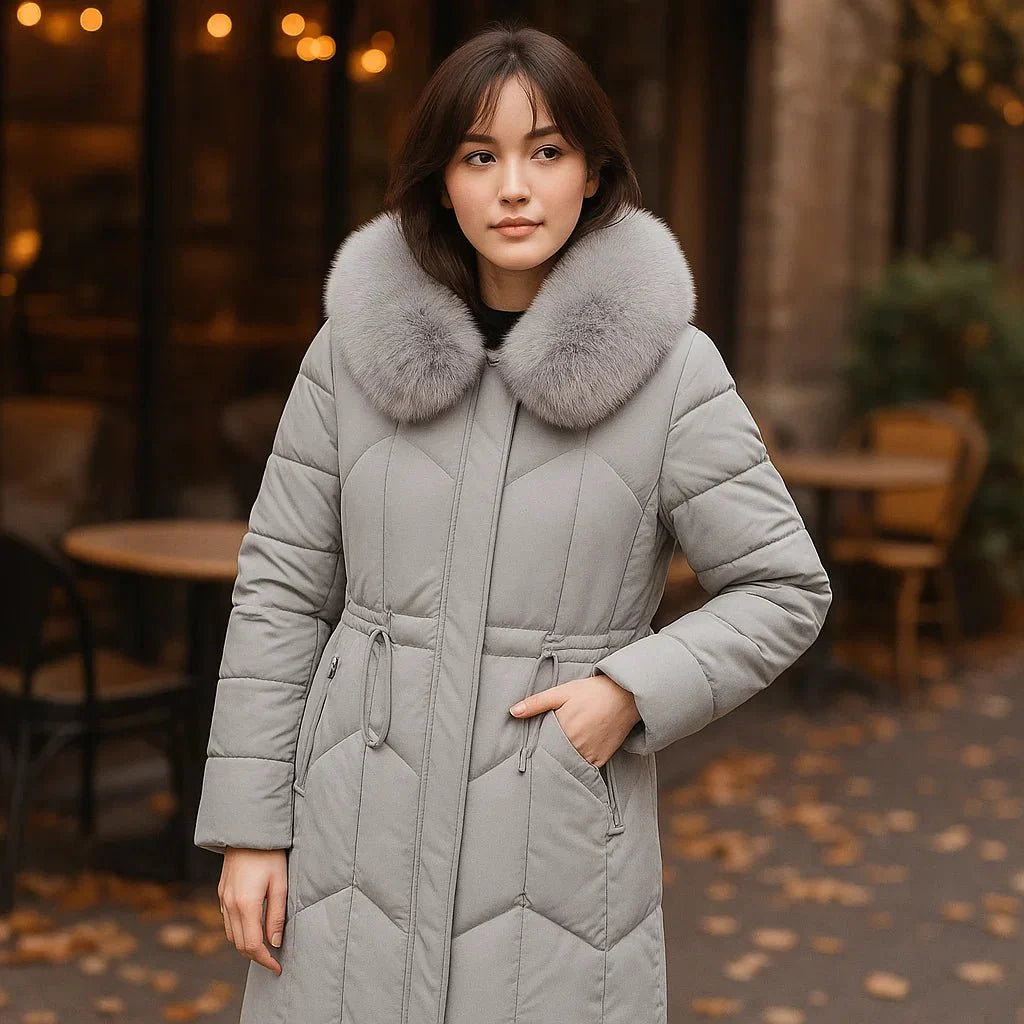 Woman wearing a gray puffer coat with a fur collar in an outdoor setting.