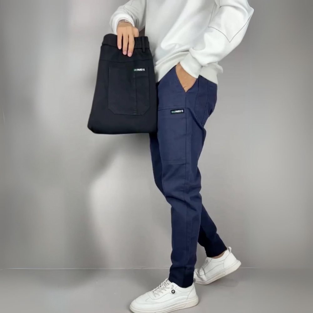 Person wearing navy pants and white sneakers holding a black bag against a gray background