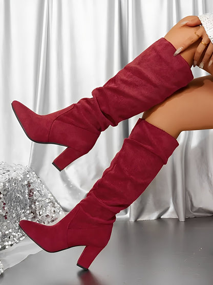 Red knee-high boots worn by a person sitting on a surface with a white curtain background.