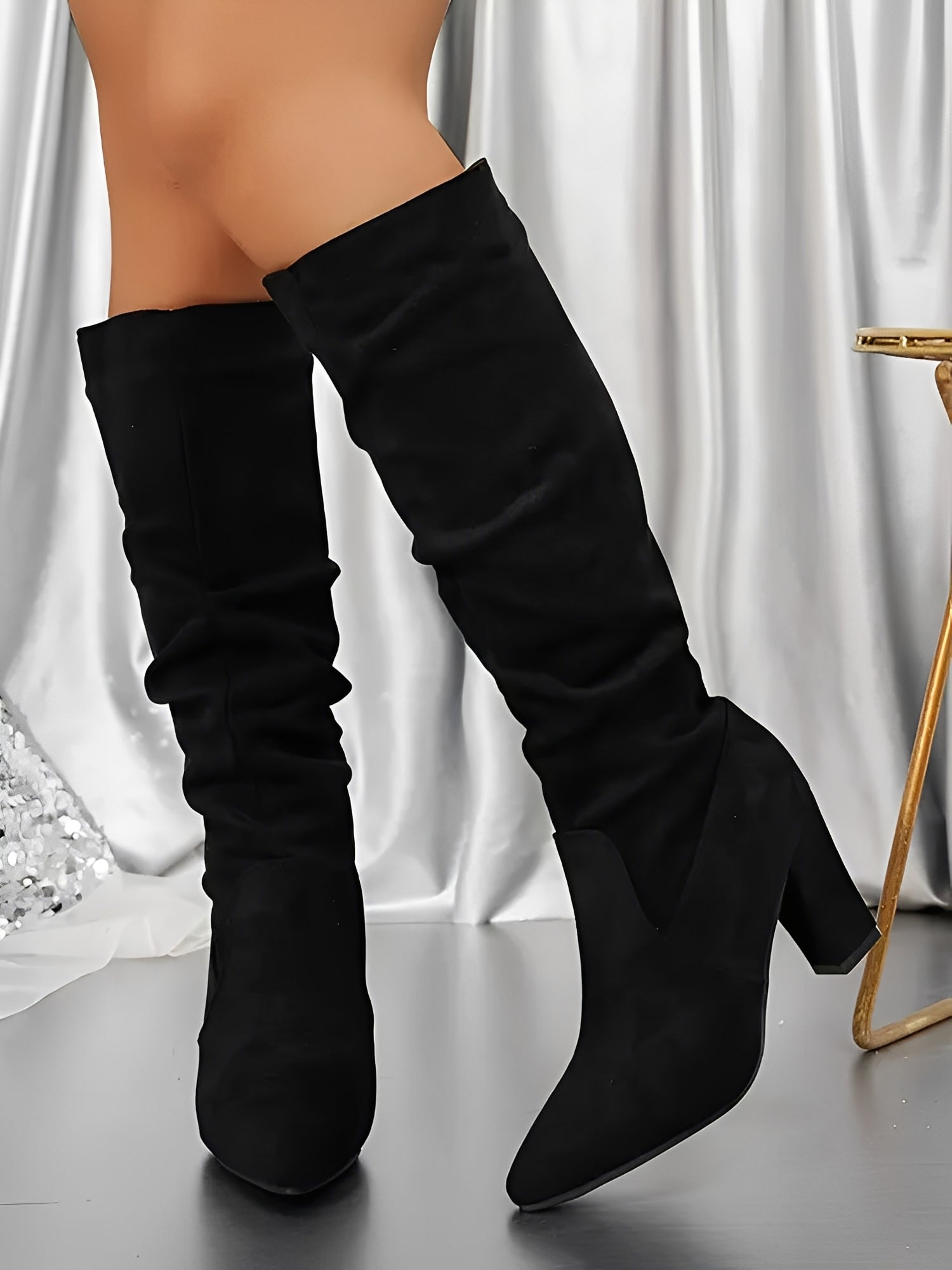 Black knee-high boots worn by a person on a neutral background