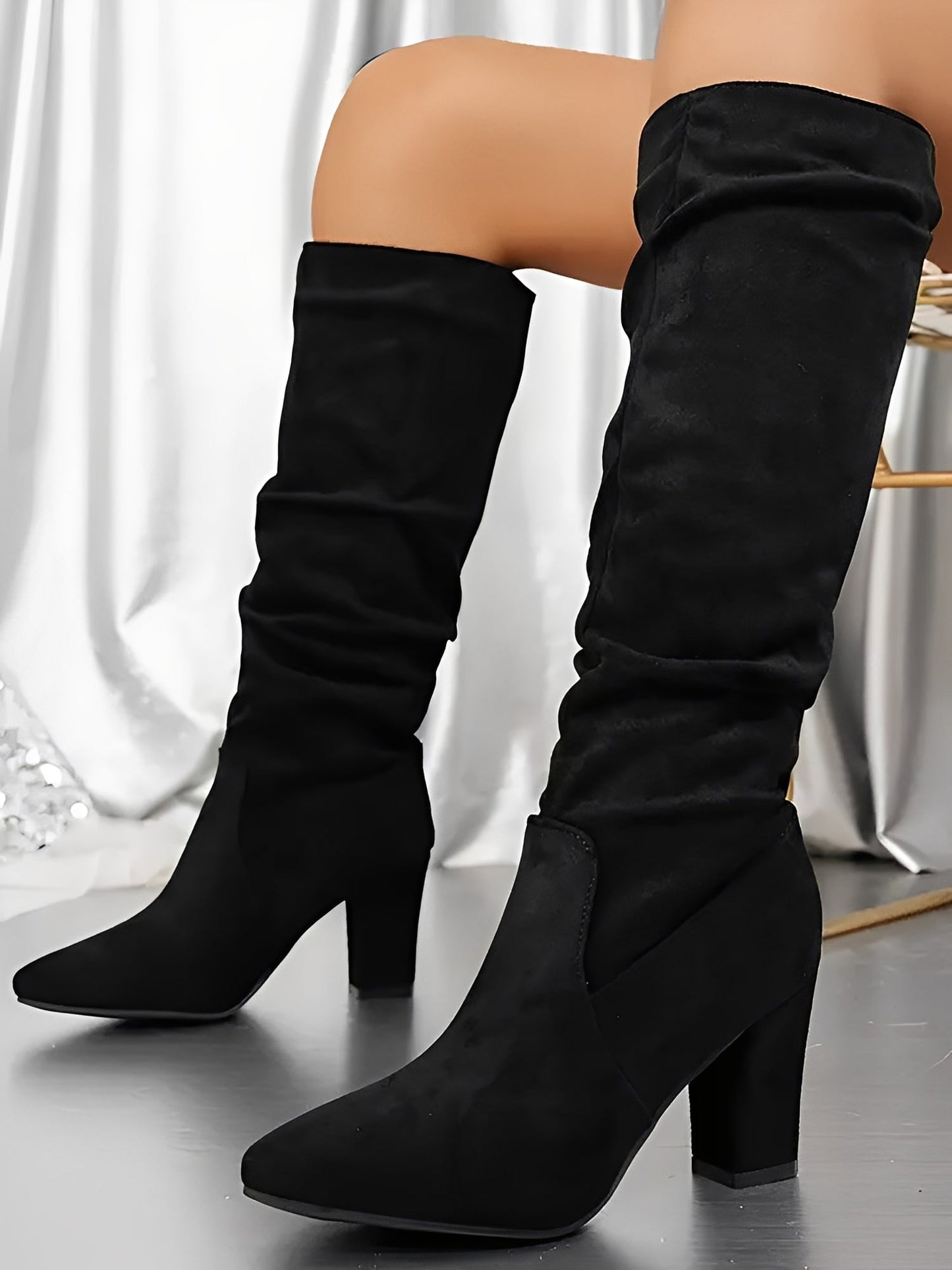 Black knee-high boots worn by a person on a neutral background
