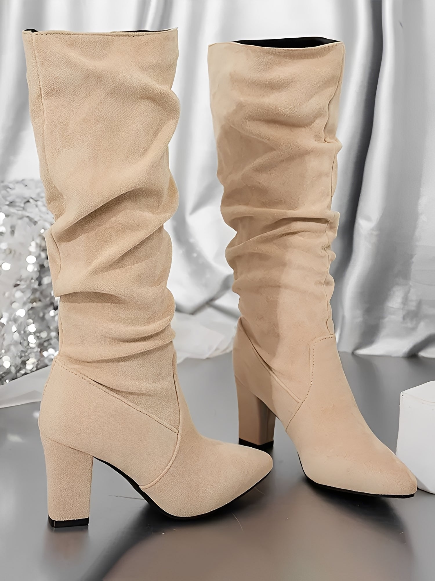 Beige knee-high boots with block heels on a reflective surface.