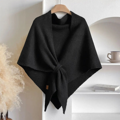 Black poncho on a hanger against a white wall with a shelf in the background.