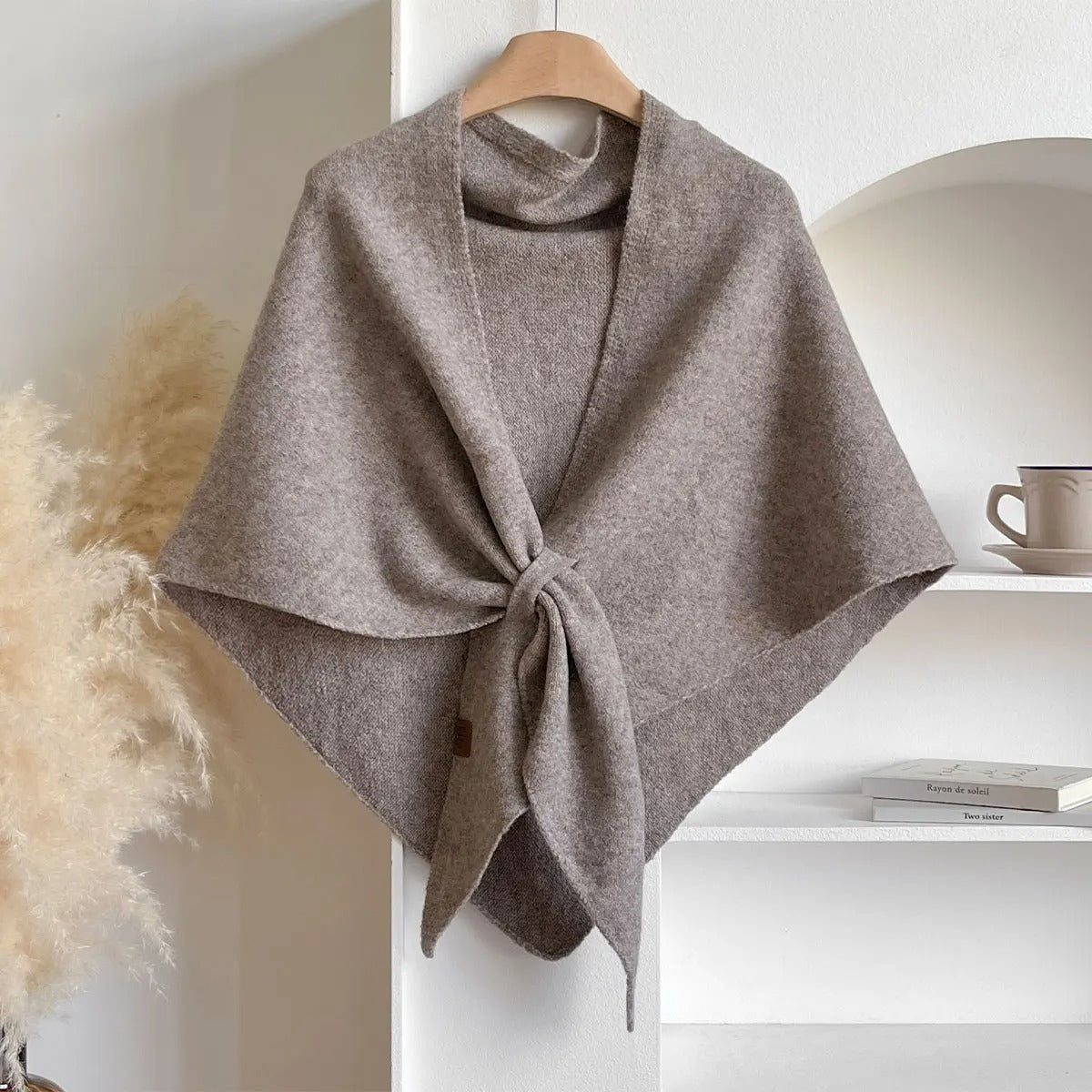 Brown poncho on a hanger against a white wall with a shelf in the background