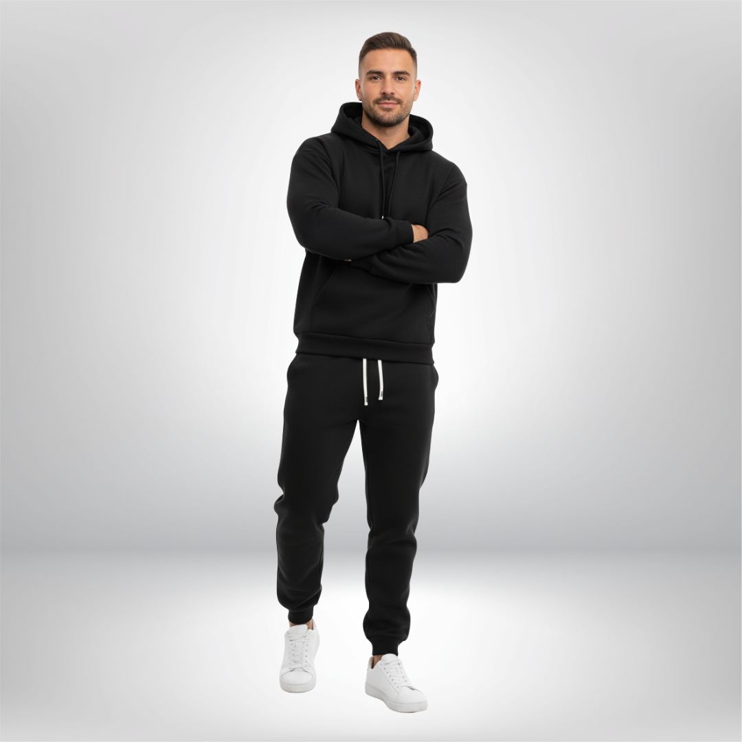 Man wearing a black hoodie and pants with white sneakers on a light gray background