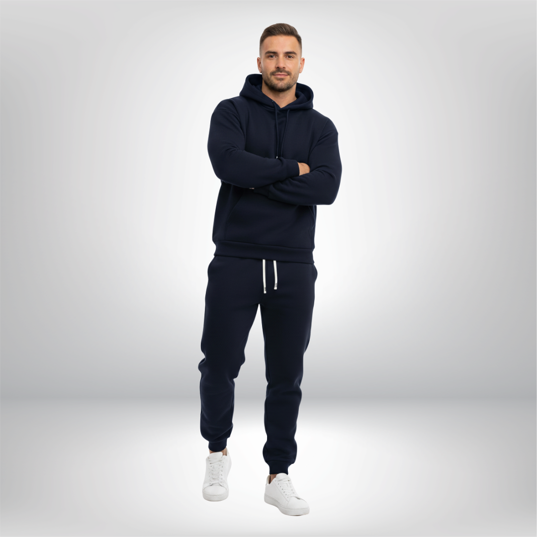 Man wearing a navy tracksuit with white shoes on a light gray background