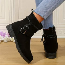 Black ankle boots with a buckle detail worn with light blue jeans on a wooden floor.