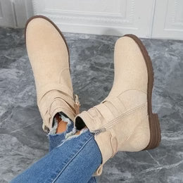 Beige ankle boots worn with blue jeans on a gray floor.