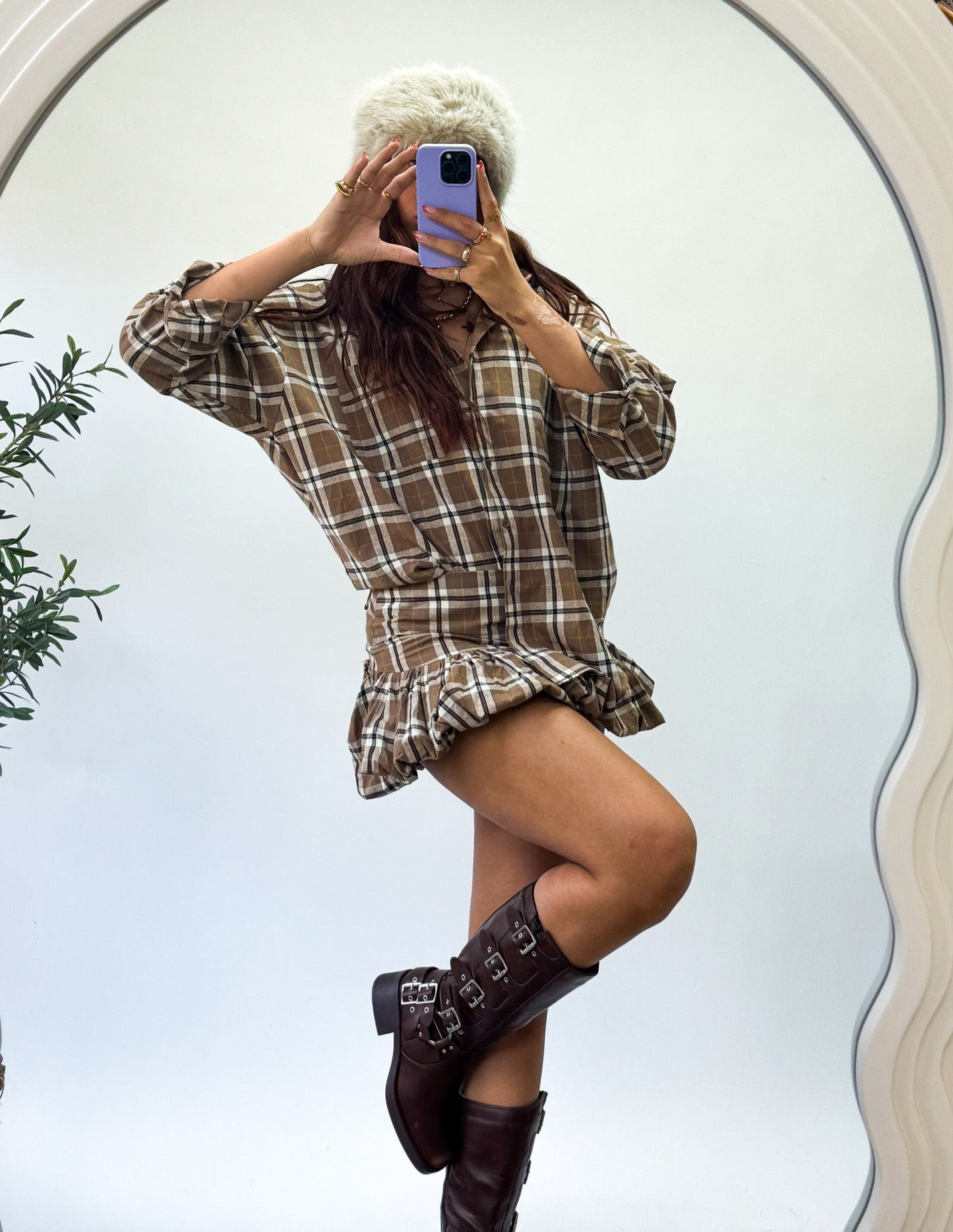 Person wearing a plaid dress and brown boots taking a mirror selfie.