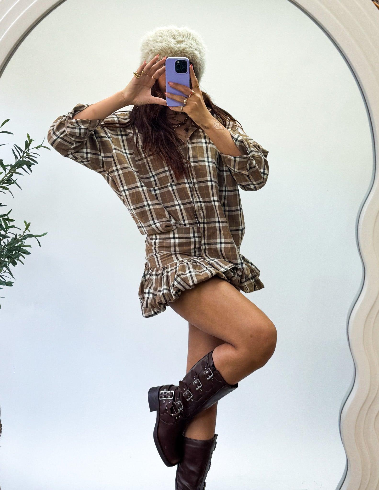 Person wearing a plaid dress and brown boots taking a mirror selfie.